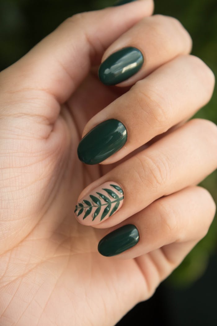 about-us Close-up of a stylish green manicure with a leaf design, showcasing glossy fingernails and natural skin tone.