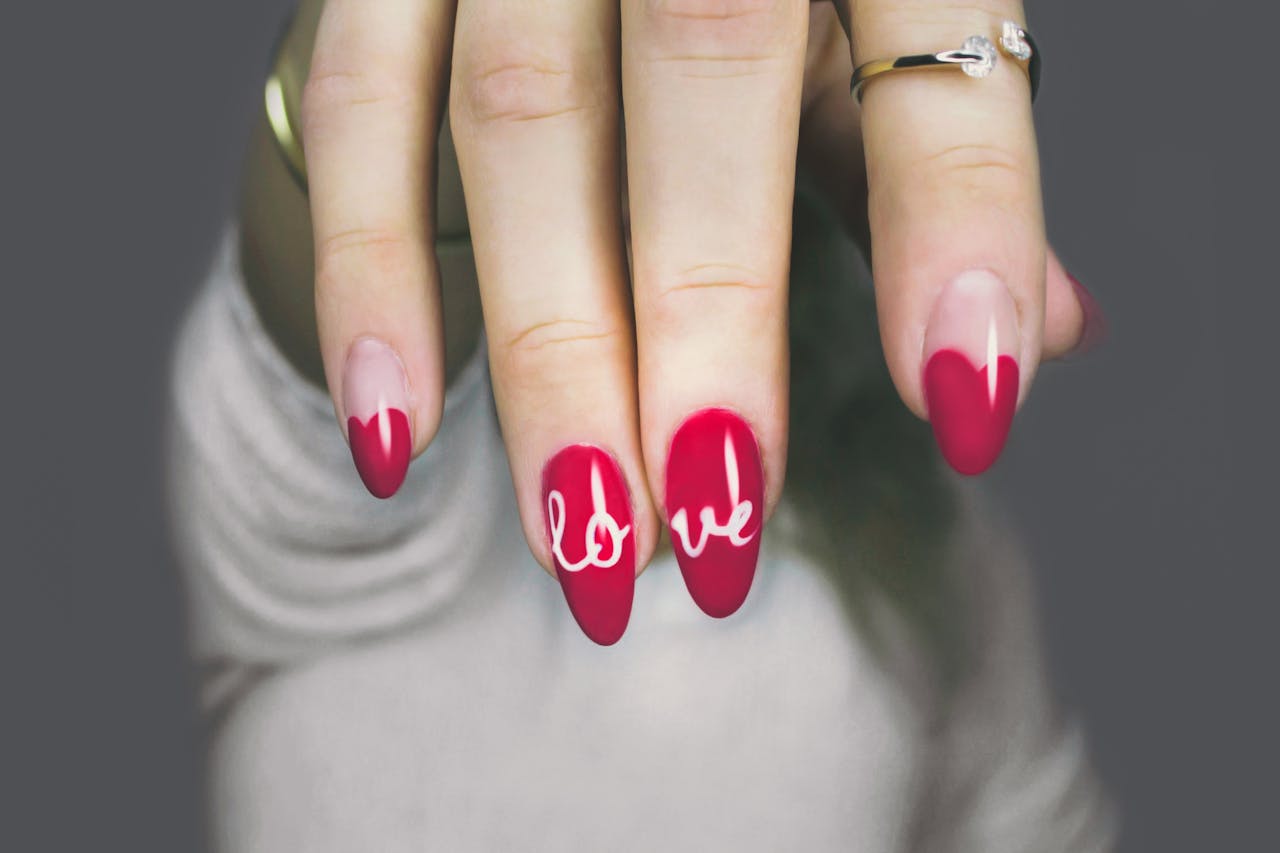 heros-img Vibrant red nails with 'love' art on a woman's hand, showcasing elegant style and design.